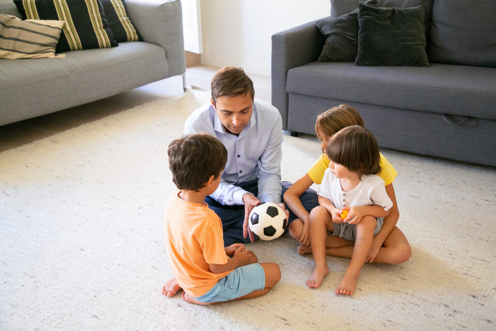 Caring dad holding ball and telling children story. Caucasian middle-aged father and kids sitting on floor in living room and playing together. Childhood, game activity and fatherhood concept